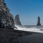 A black sand beach with a rock formation in the background