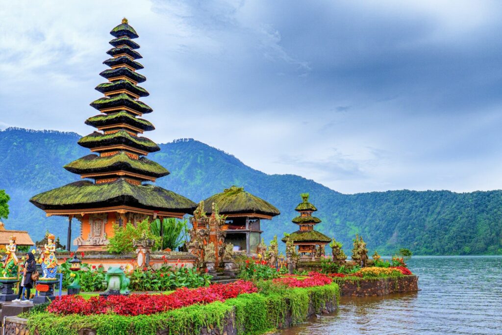 Templo marrom e verde perto de um lago e montanha verde sob um céu azul durante o dia
