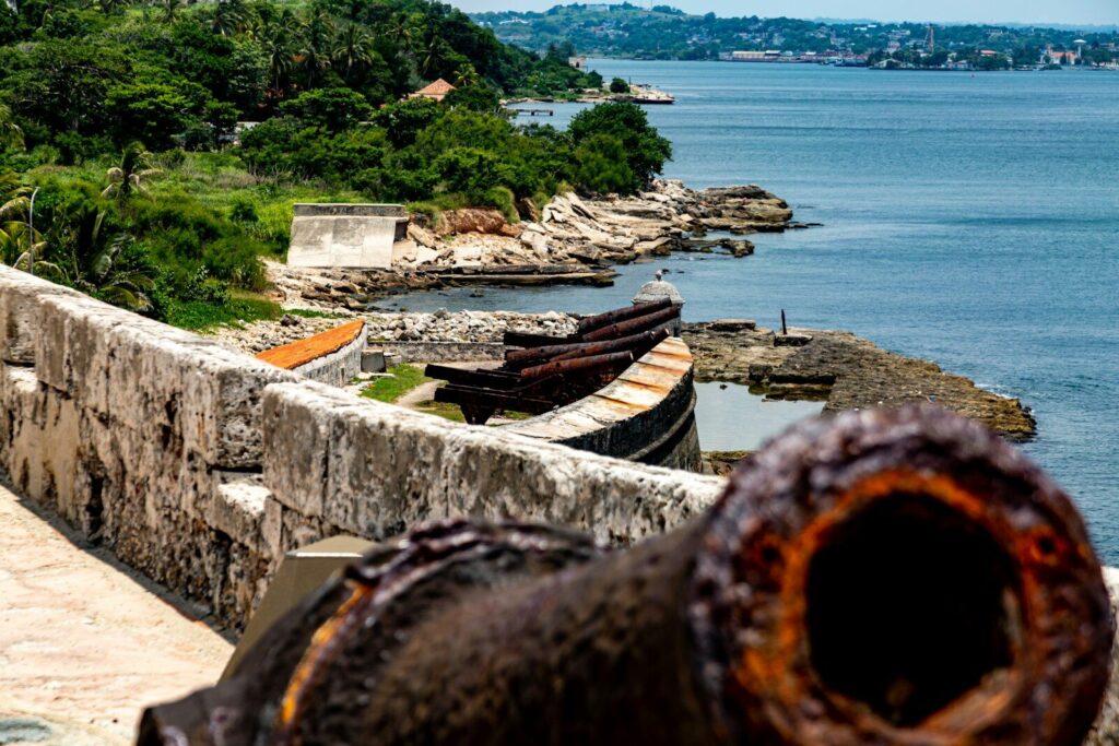 Canhões antigos em um forte de pedra com vista para uma baía.