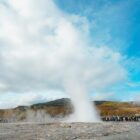 Geyser erupting with steam against a cloudy blue sky