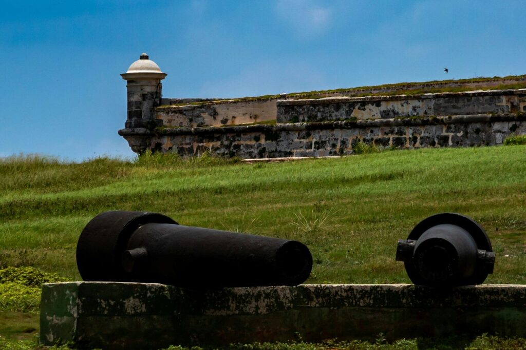 Um antigo canhão preto está posicionado em frente a um forte de pedra histórico.