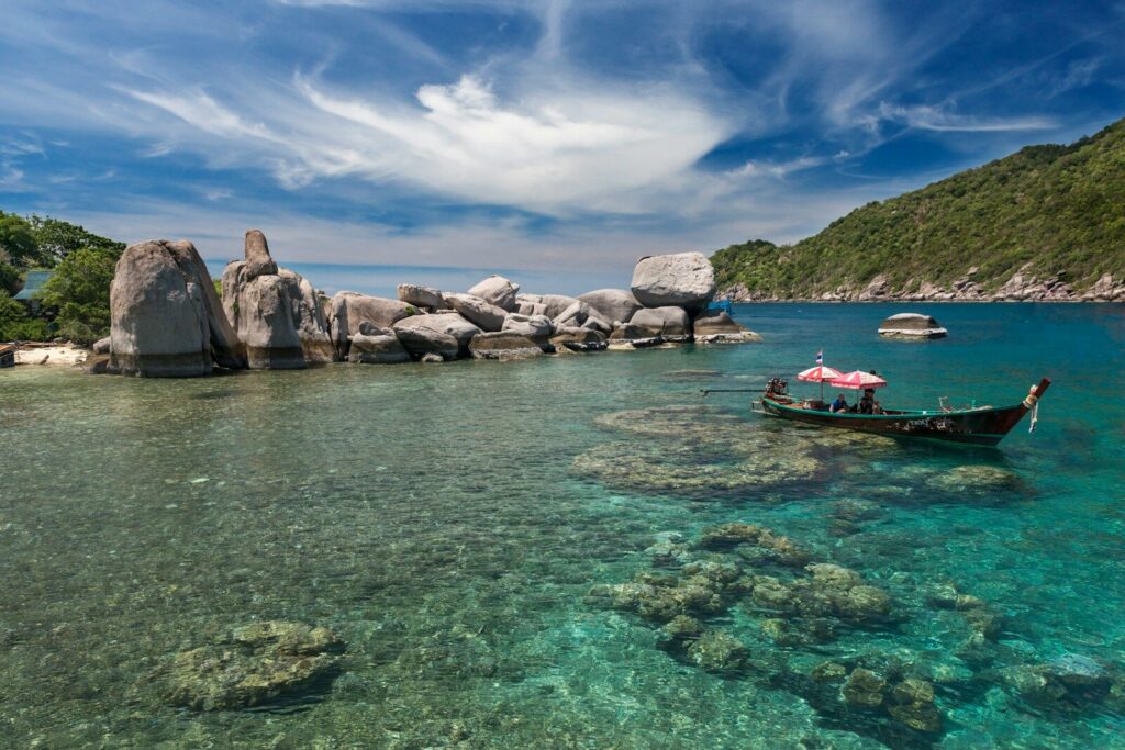 Granite boulders and a longtail boat in clear shallow water off Koh Tao