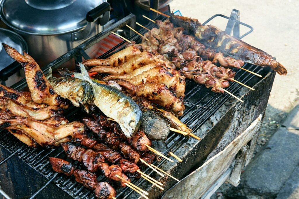 Fish and meat grilling over coals at a street food stall