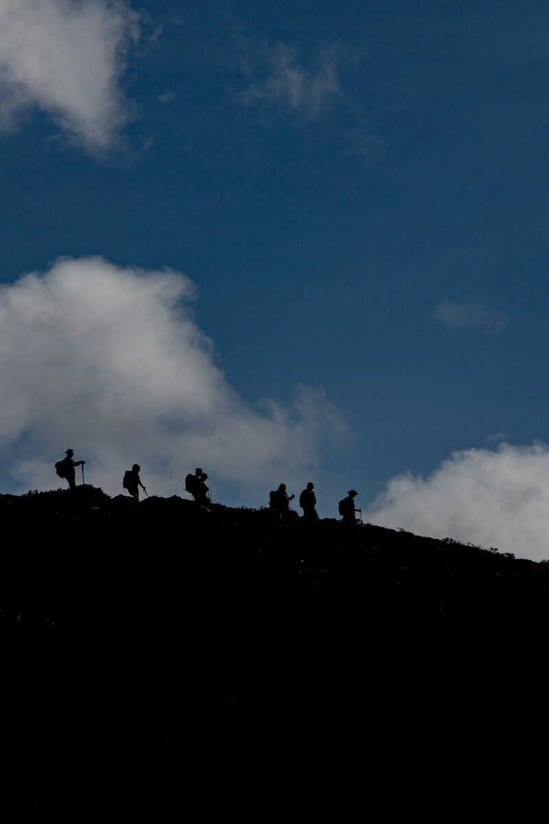 Silhouetted hikers ascend a mountain ridge under a cloudy sky