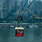 Red cable car crosses river, towering city skyline in background