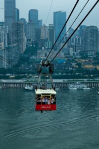 Red cable car crosses river, towering city skyline in background