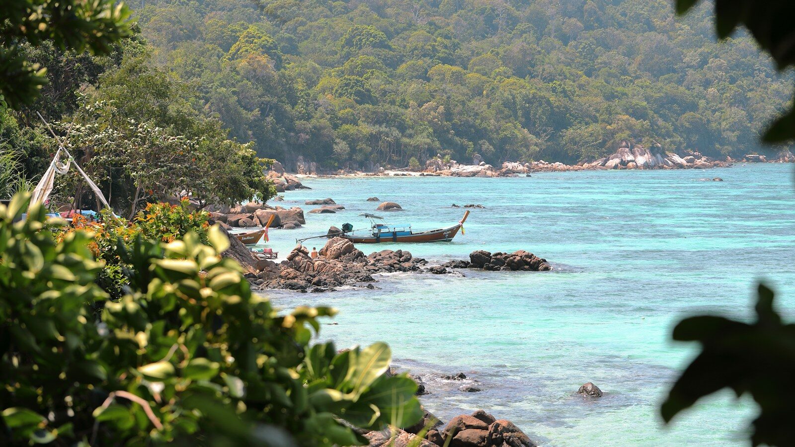 Longtail boat moored in a turquoise bay beside granite rocks on Koh Lipe, Thailand