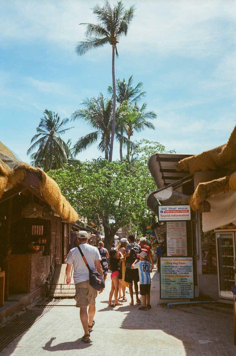 People strolling past thatched shops on a tropical walking street in Koh Lipe, Thailand