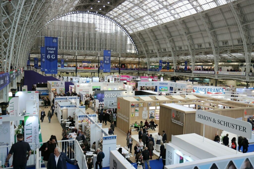 A busy trade fair hall seen from above, with rows of exhibition stands and visitors