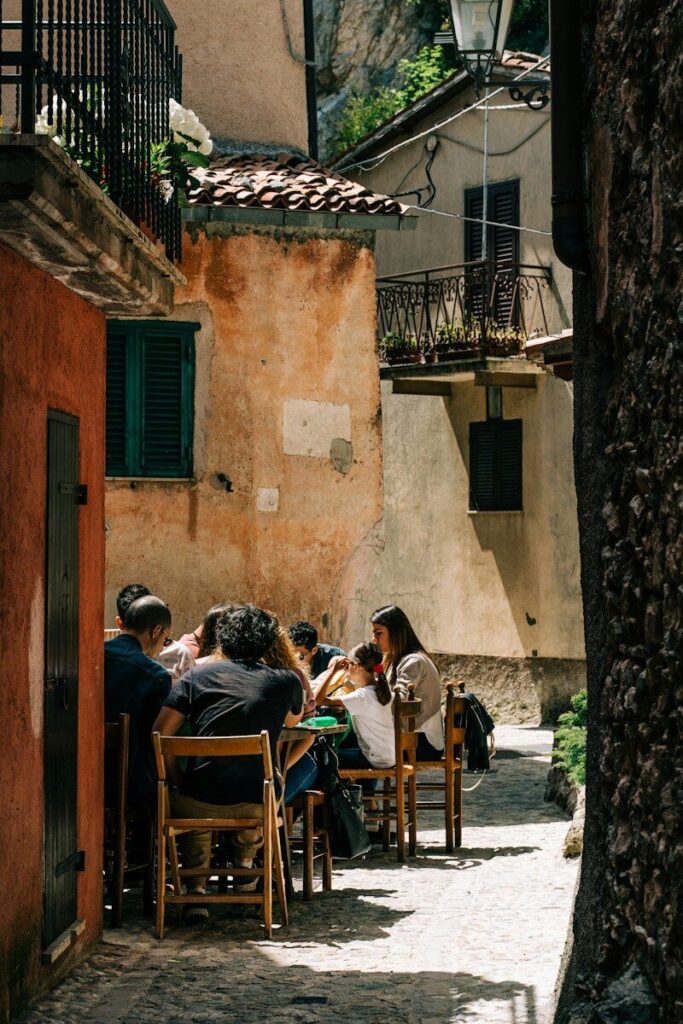 Diners at outdoor tables in a narrow sunlit alley at lunchtime