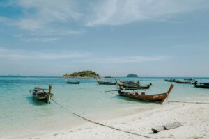 Turquoise water and longtail boats lined up along a white sand beach on Koh Lipe