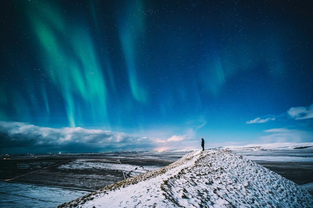 A lone figure on a snowy ridge under the northern lights in Iceland